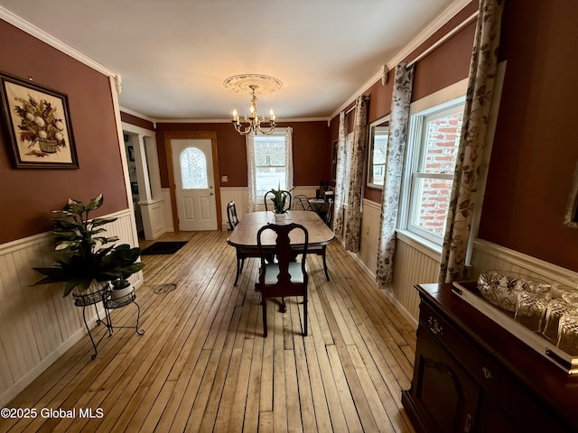 dining space with light hardwood / wood-style floors, ornamental molding, and a notable chandelier