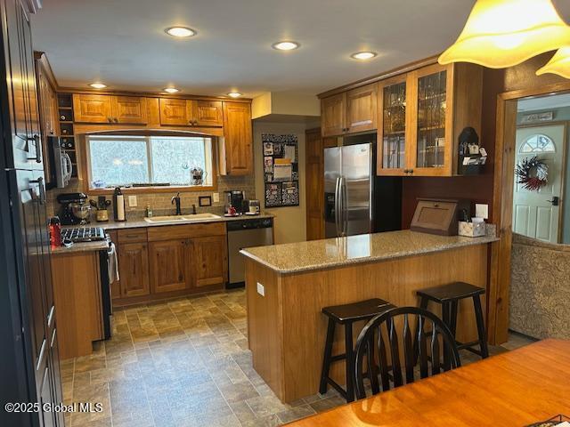 kitchen featuring light stone countertops, sink, stainless steel appliances, kitchen peninsula, and a breakfast bar