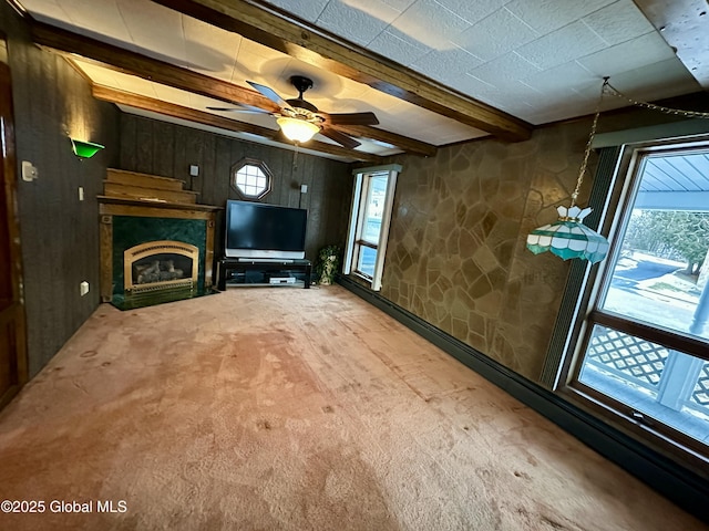 unfurnished living room with beamed ceiling, a healthy amount of sunlight, carpet flooring, and ceiling fan