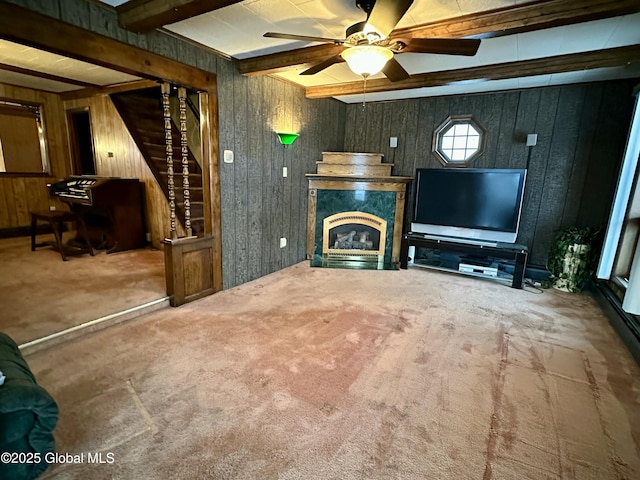 unfurnished living room featuring ceiling fan, carpet floors, beam ceiling, and wood walls