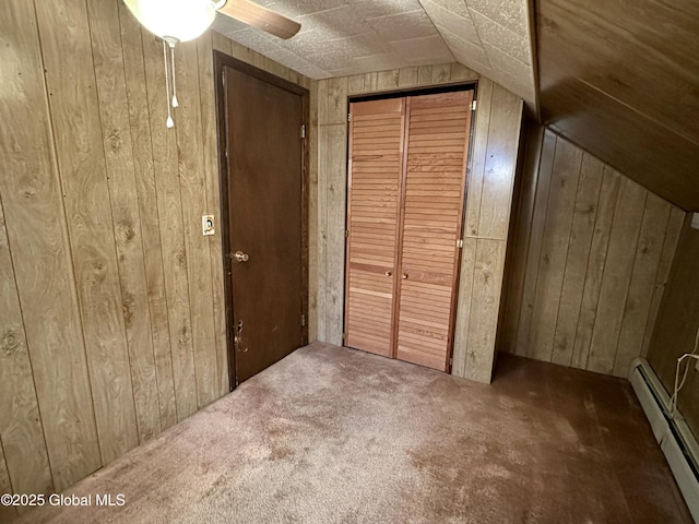 unfurnished bedroom featuring vaulted ceiling, dark carpet, wooden walls, and baseboard heating