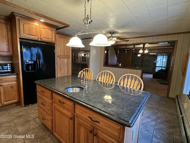 kitchen featuring sink, dark stone countertops, a baseboard radiator, an island with sink, and black refrigerator with ice dispenser