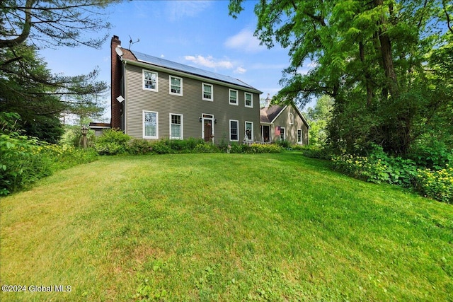 rear view of house featuring a lawn and solar panels