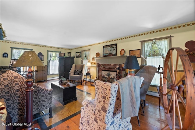 living room featuring a brick fireplace, a healthy amount of sunlight, a baseboard heating unit, and hardwood / wood-style flooring