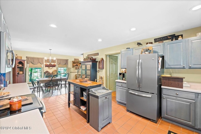 kitchen featuring stainless steel fridge, light tile patterned floors, pendant lighting, an inviting chandelier, and gray cabinets