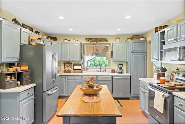 kitchen featuring sink, light tile patterned flooring, hanging light fixtures, and appliances with stainless steel finishes