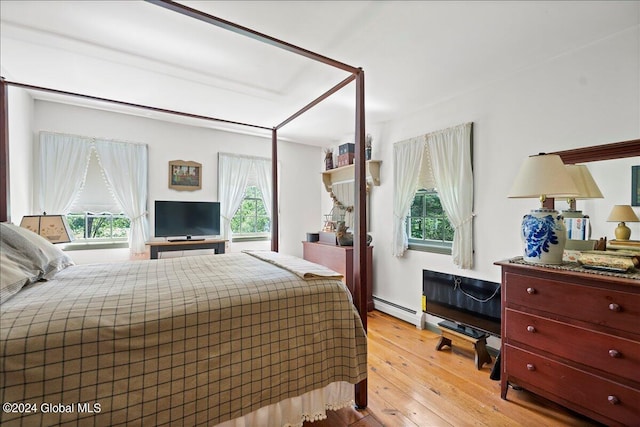 bedroom featuring light hardwood / wood-style floors, baseboard heating, and multiple windows