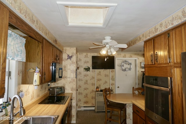 kitchen featuring sink, oven, a baseboard heating unit, ceiling fan, and black electric cooktop