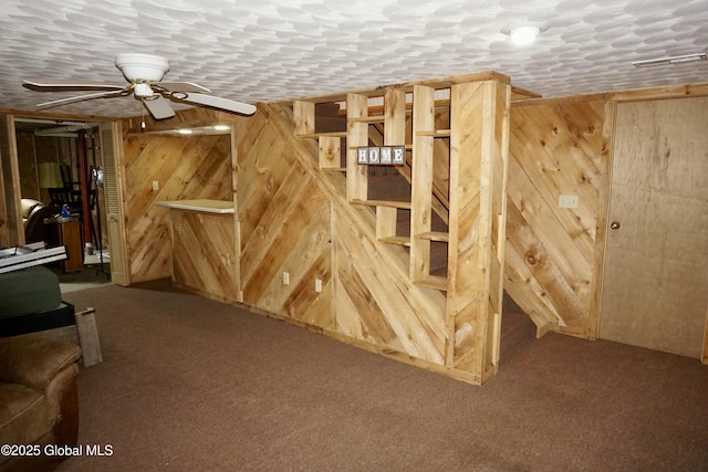 basement with ceiling fan, carpet floors, a textured ceiling, and wood walls