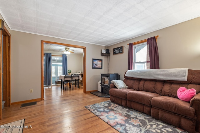 living room with ceiling fan, light hardwood / wood-style flooring, crown molding, and a wood stove