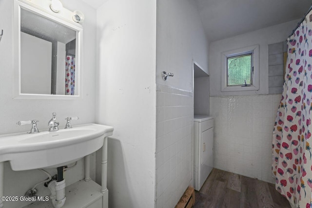 bathroom featuring a shower with shower curtain, sink, tile walls, hardwood / wood-style floors, and washer / dryer