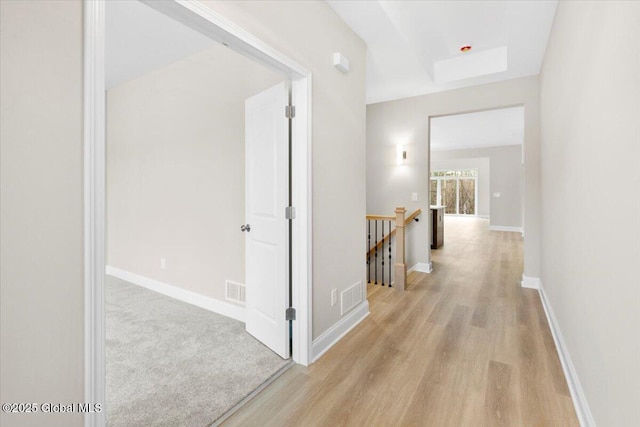 corridor featuring visible vents, light wood-style flooring, an upstairs landing, and baseboards