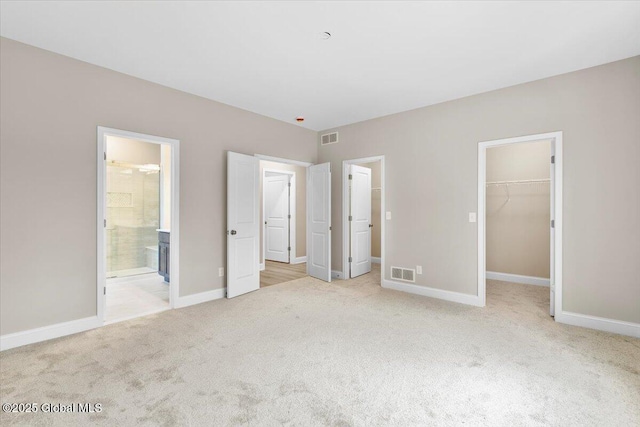 unfurnished bedroom with light carpet, a spacious closet, visible vents, and baseboards