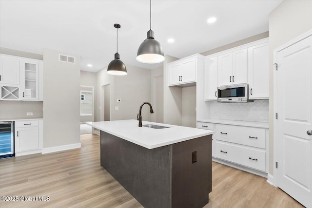 kitchen featuring a sink, visible vents, light wood-type flooring, decorative backsplash, and stainless steel microwave