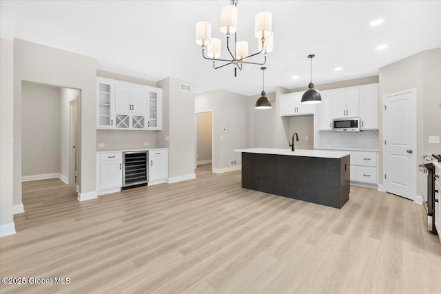 kitchen featuring beverage cooler, stainless steel microwave, light wood-style flooring, and white cabinets