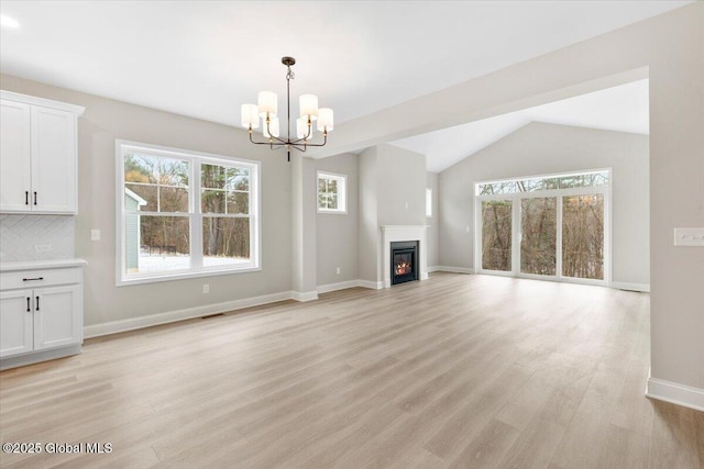 unfurnished living room featuring light wood-style floors, baseboards, vaulted ceiling, and a glass covered fireplace