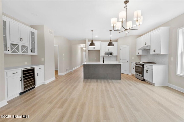 kitchen featuring wine cooler, decorative backsplash, appliances with stainless steel finishes, light wood-style floors, and under cabinet range hood