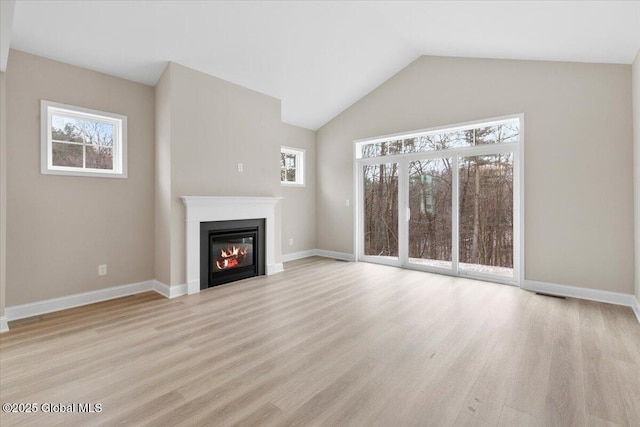 unfurnished living room featuring light wood-style floors, a glass covered fireplace, vaulted ceiling, and baseboards