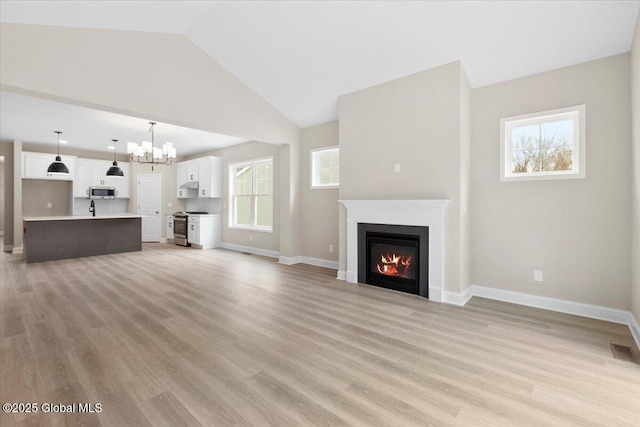 unfurnished living room with a glass covered fireplace, baseboards, lofted ceiling, and light wood finished floors