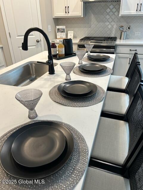 interior space featuring tasteful backsplash, light countertops, stainless steel range with gas cooktop, white cabinetry, and a sink