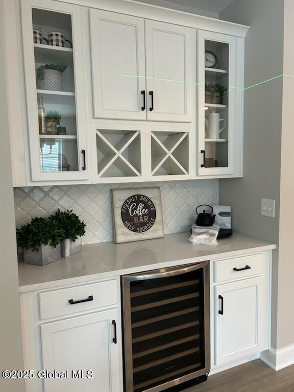 bar with dark wood-style floors, a bar, wine cooler, and decorative backsplash