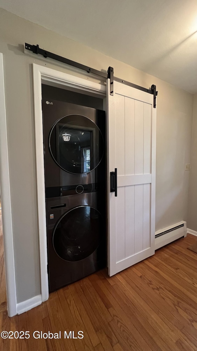 washroom with a barn door, wood-type flooring, stacked washer / dryer, and a baseboard heating unit