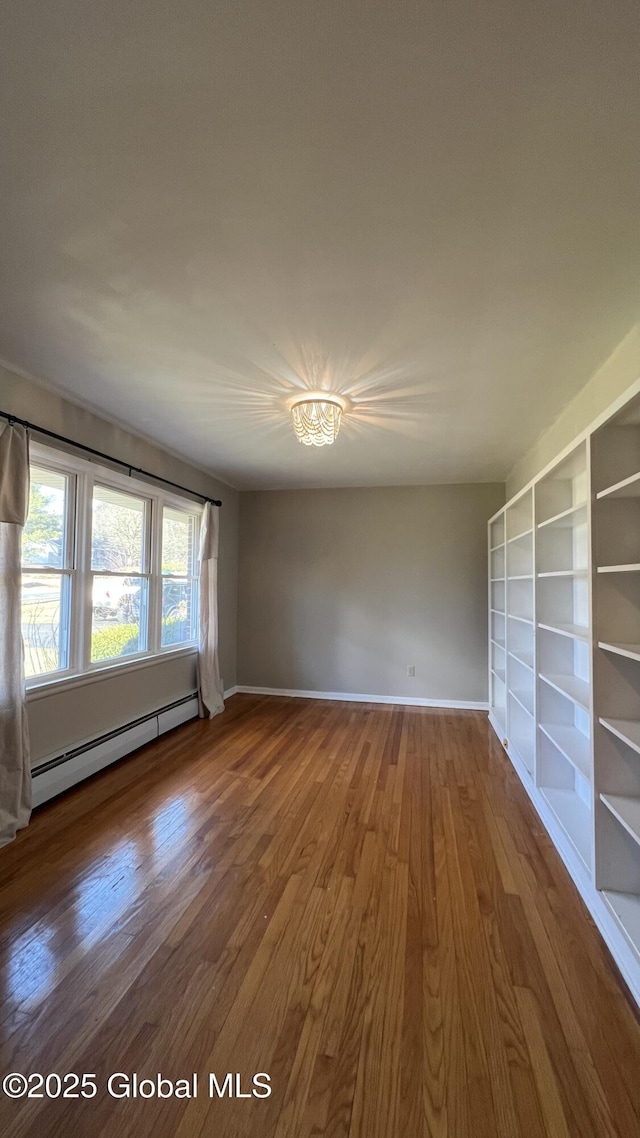 spare room with hardwood / wood-style flooring, a notable chandelier, baseboard heating, and built in shelves