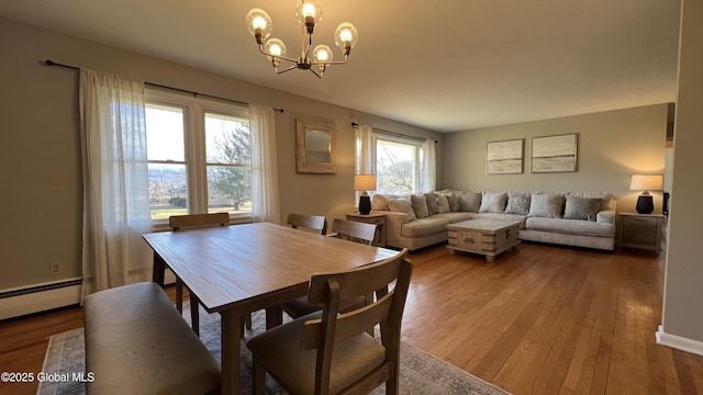 dining space with hardwood / wood-style flooring, baseboard heating, a wealth of natural light, and an inviting chandelier