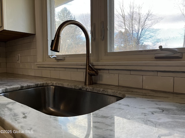 room details with decorative backsplash, light stone counters, and sink