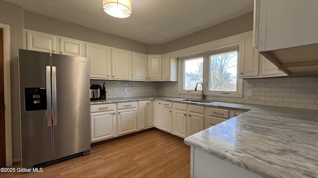 kitchen featuring white cabinetry, sink, backsplash, stainless steel fridge, and light hardwood / wood-style floors