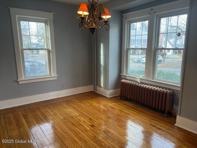 unfurnished dining area with radiator heating unit, wood-type flooring, and an inviting chandelier