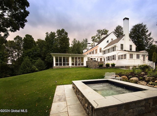 back house at dusk featuring a sunroom, a lawn, and a hot tub