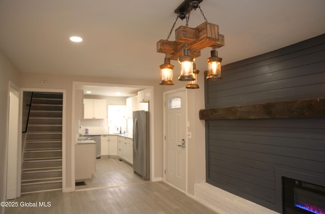 interior space with backsplash, decorative light fixtures, light hardwood / wood-style floors, white cabinetry, and stainless steel refrigerator