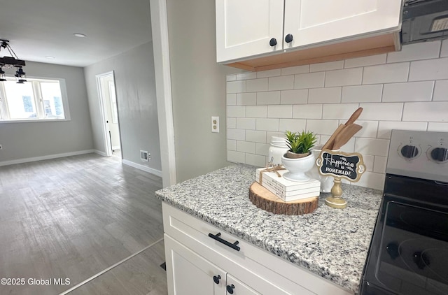 kitchen with tasteful backsplash, electric stove, light stone counters, and white cabinets