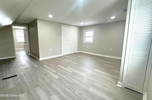 unfurnished bedroom with light wood-type flooring and vaulted ceiling