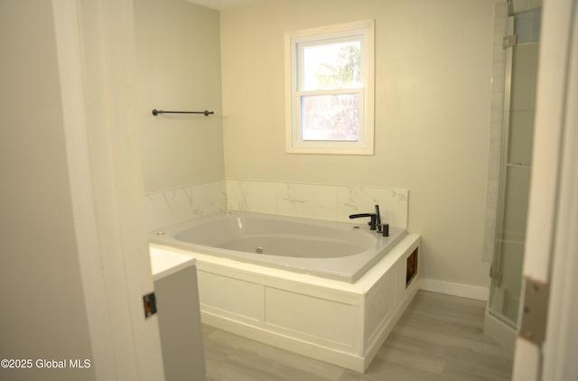 bathroom featuring wood-type flooring and a relaxing tiled tub