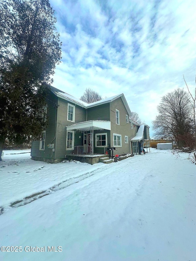 snow covered rear of property featuring covered porch