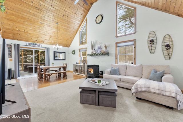 living room with wooden ceiling, light colored carpet, high vaulted ceiling, a wood stove, and an inviting chandelier