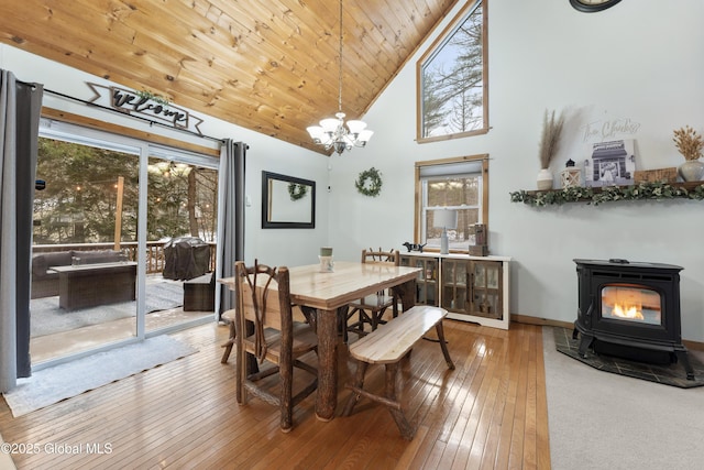 dining room featuring a chandelier, plenty of natural light, high vaulted ceiling, and a wood stove