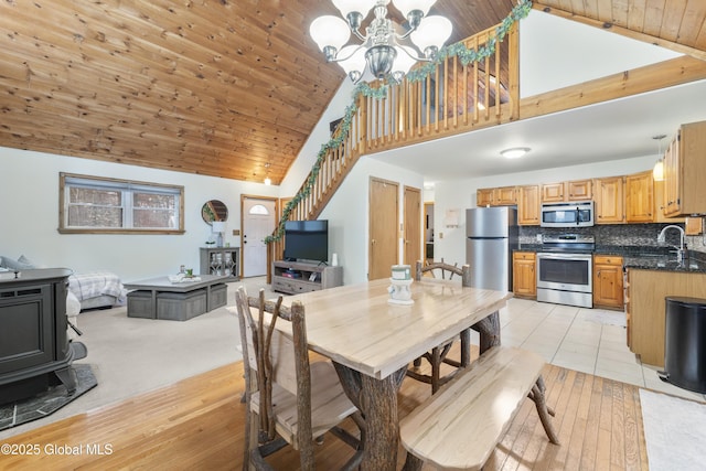 dining area with wood ceiling, a wood stove, high vaulted ceiling, an inviting chandelier, and sink