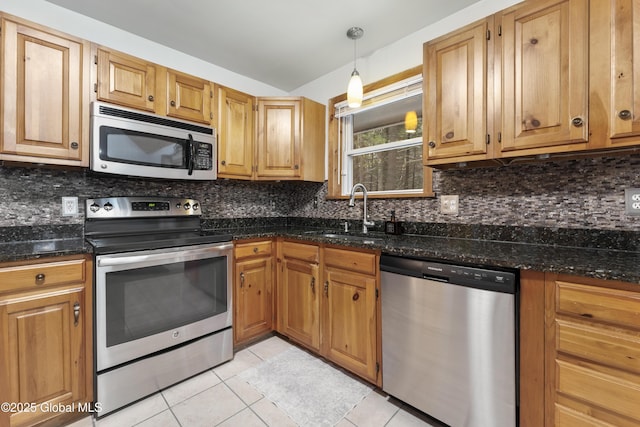 kitchen with hanging light fixtures, dark stone counters, appliances with stainless steel finishes, light tile patterned flooring, and sink