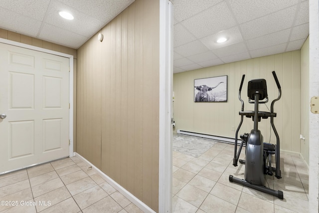 exercise area with a baseboard heating unit, wooden walls, and a paneled ceiling