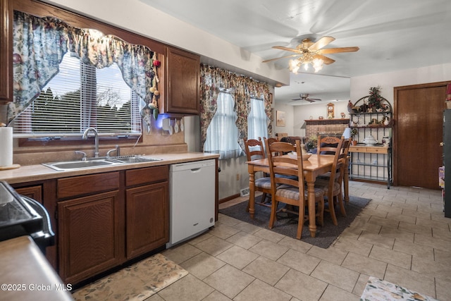 kitchen with a fireplace, sink, light tile patterned floors, ceiling fan, and white dishwasher