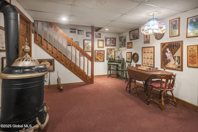 interior space with carpet flooring, a drop ceiling, and a wood stove