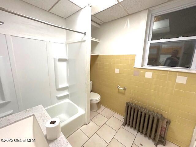 full bathroom featuring a drop ceiling, radiator, bathing tub / shower combination, tile patterned floors, and toilet