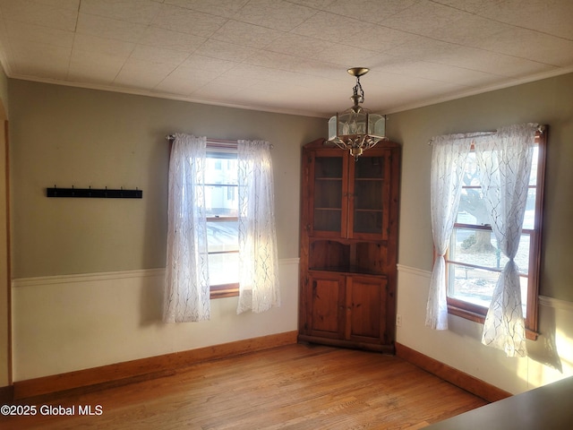 unfurnished dining area with light wood-type flooring, baseboards, a chandelier, and crown molding