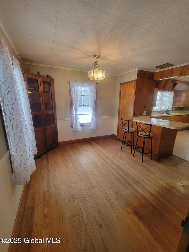 kitchen with brown cabinets, light countertops, light wood-style floors, a peninsula, and a kitchen bar