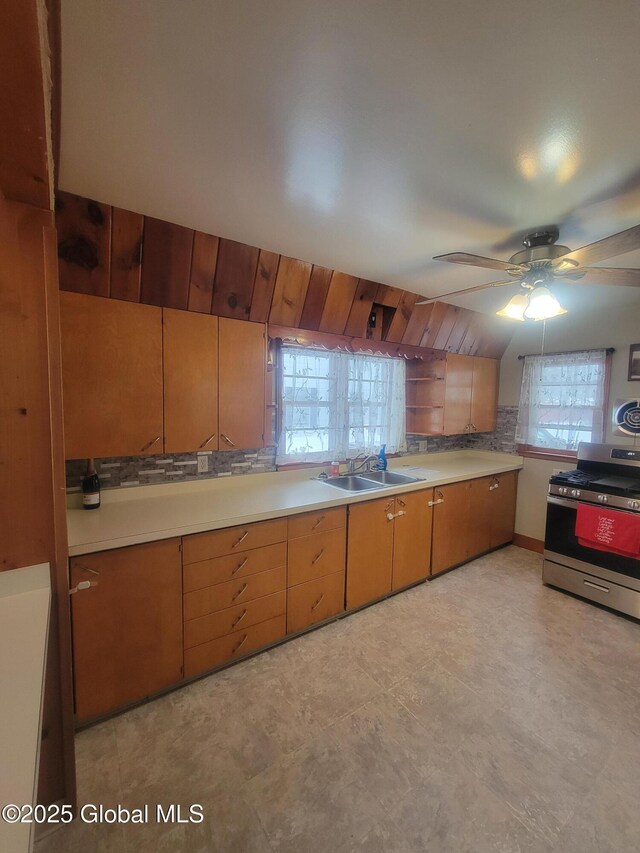 kitchen featuring a ceiling fan, gas range, brown cabinets, light countertops, and a sink