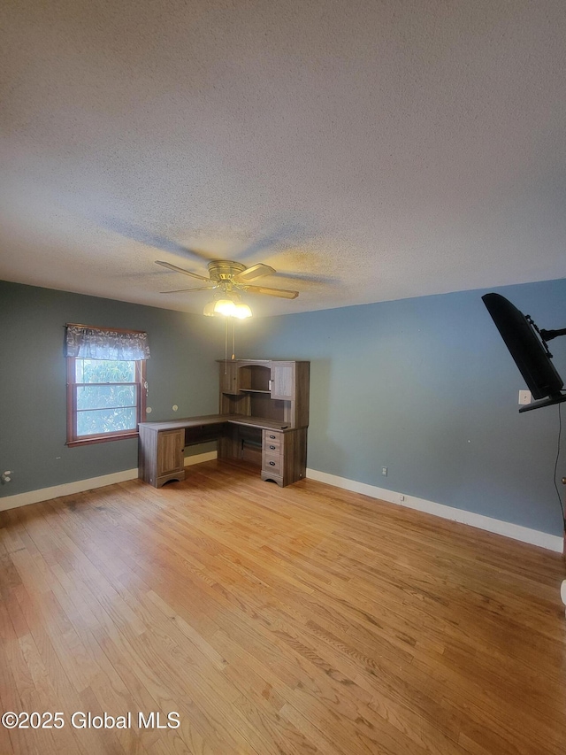 unfurnished office featuring light wood-style flooring, baseboards, and a textured ceiling