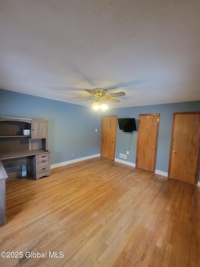 unfurnished living room with a textured ceiling, ceiling fan, light wood-style flooring, visible vents, and baseboards